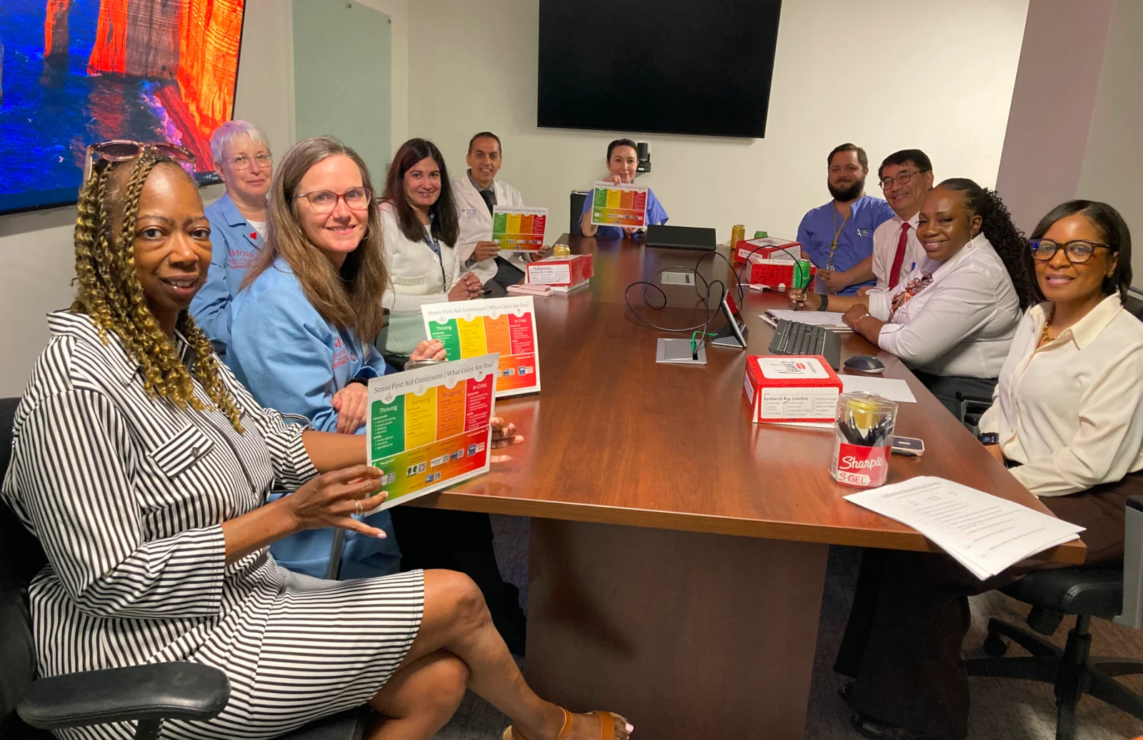 Emory Healthcare staff gathered around a conference table during a Stress First Aid session, with several participants holding up printed Stress First Aid Continuum cards.